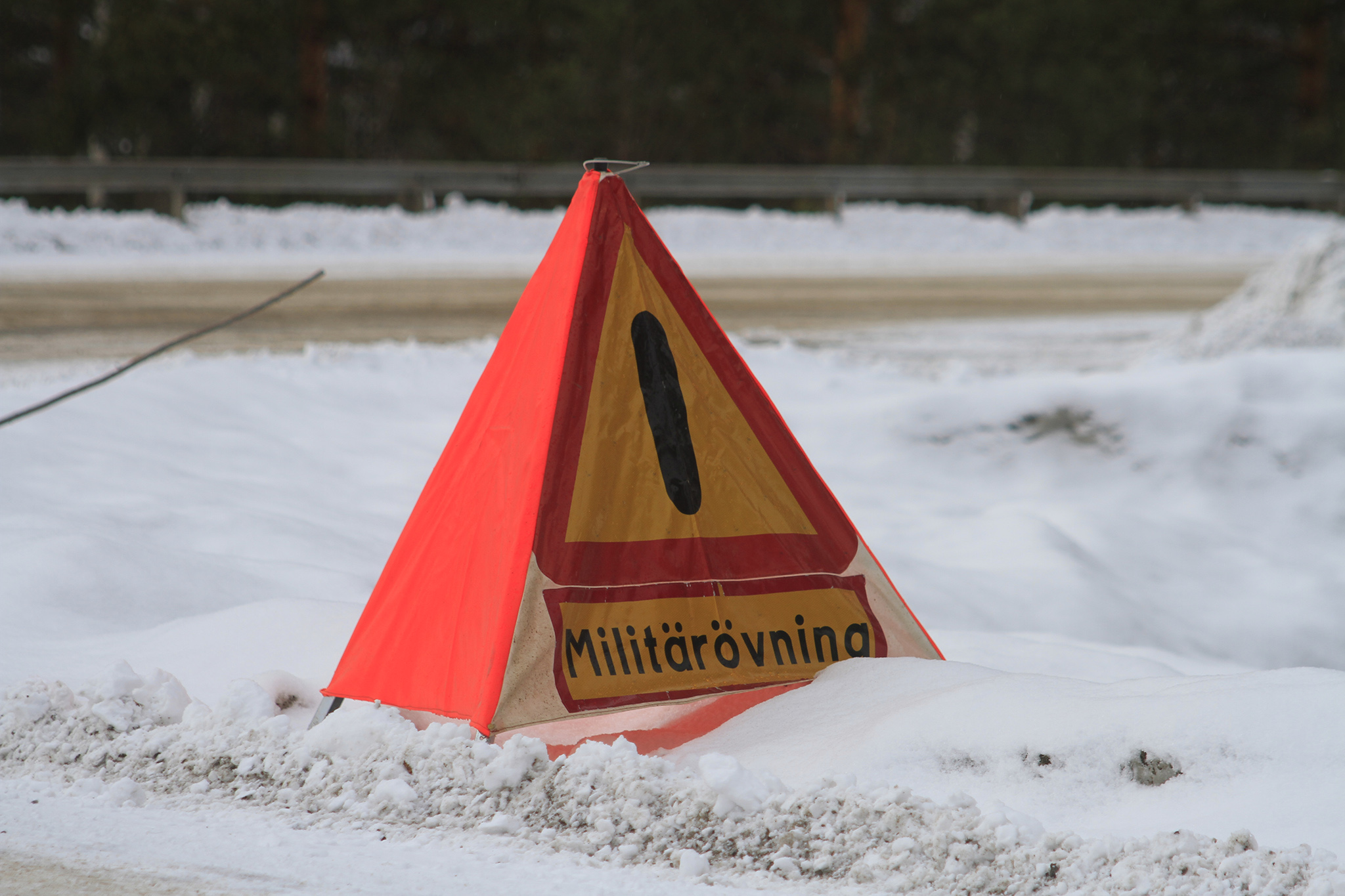 gul och röd varningstriangel i med texten militärövning står vid sidan av en snöig väg
