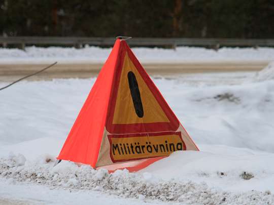 gul och röd varningstriangel i med texten militärövning står vid sidan av en snöig väg