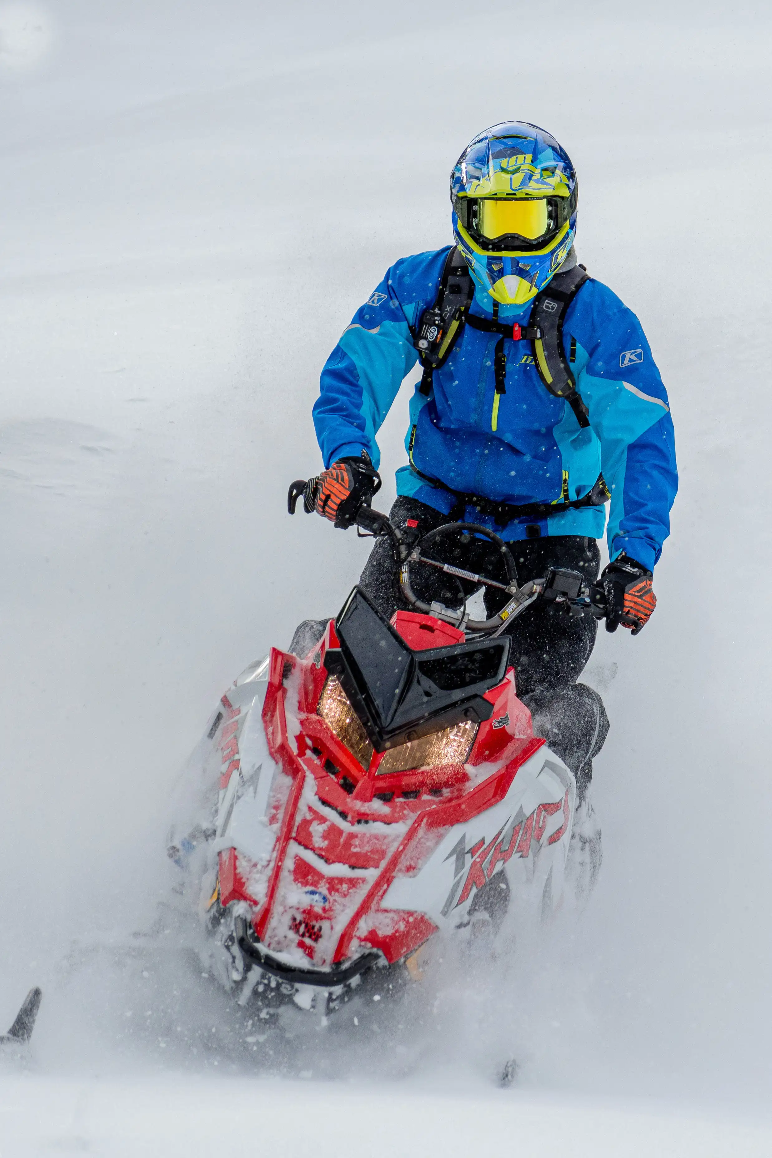 en röd snöskoter körs i snö av förare med blå klädsel