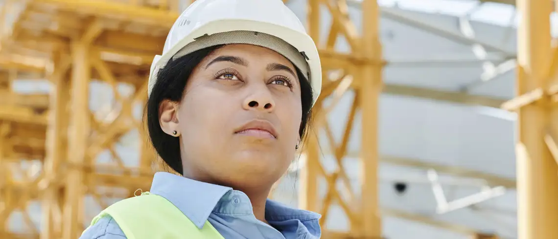 bild som visar mörkhårigkvinna med hjälm på byggarbetsplats