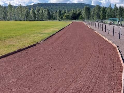 bilden visar en löparbana med röd sand med skog och blå himmel i bakgrunden