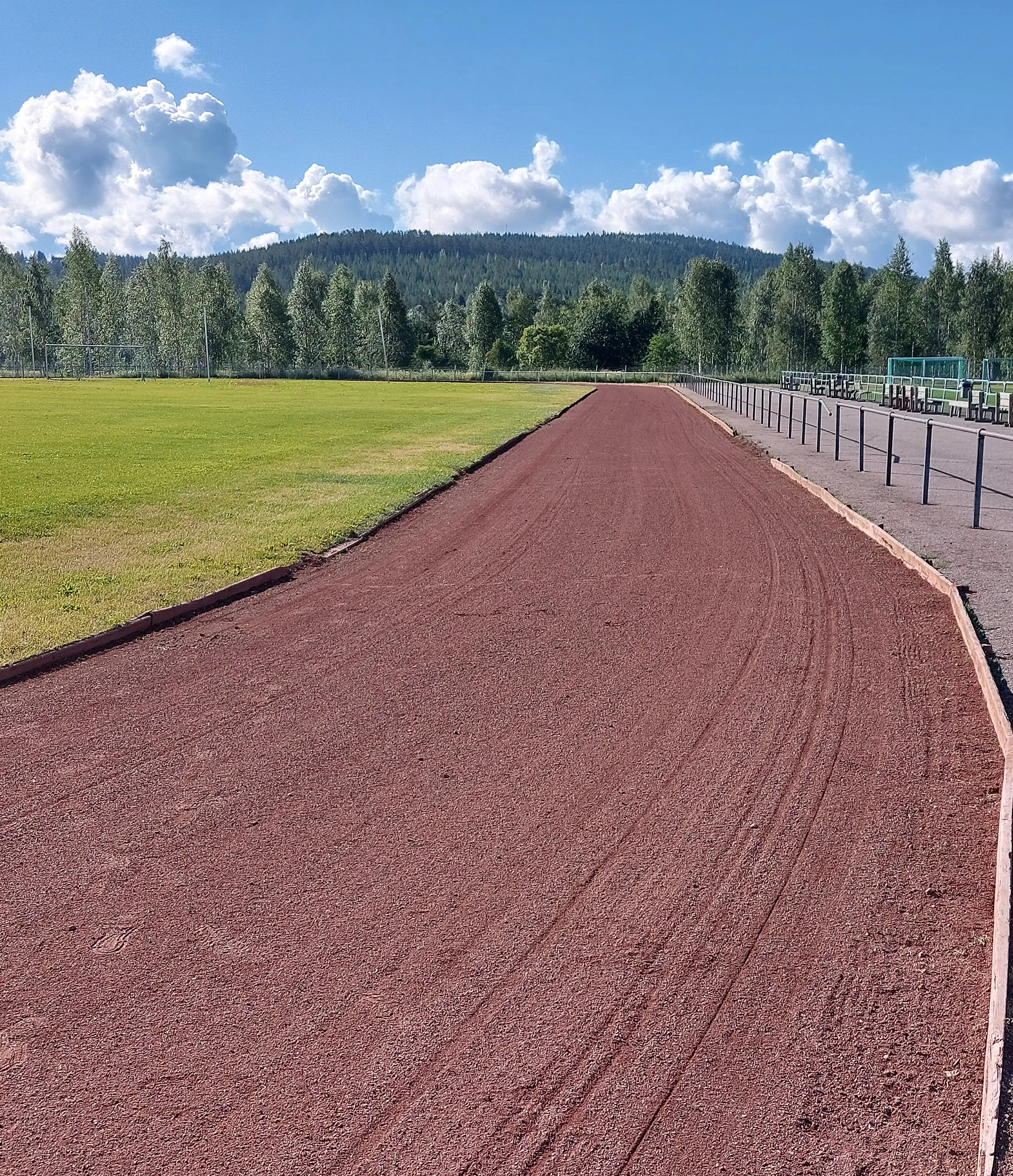 bilden visar en löparbana med röd sand med skog och blå himmel i bakgrunden