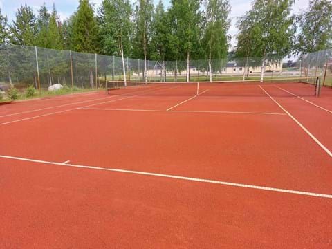Bilden visar en tennisbana omgiven av gröna björkar