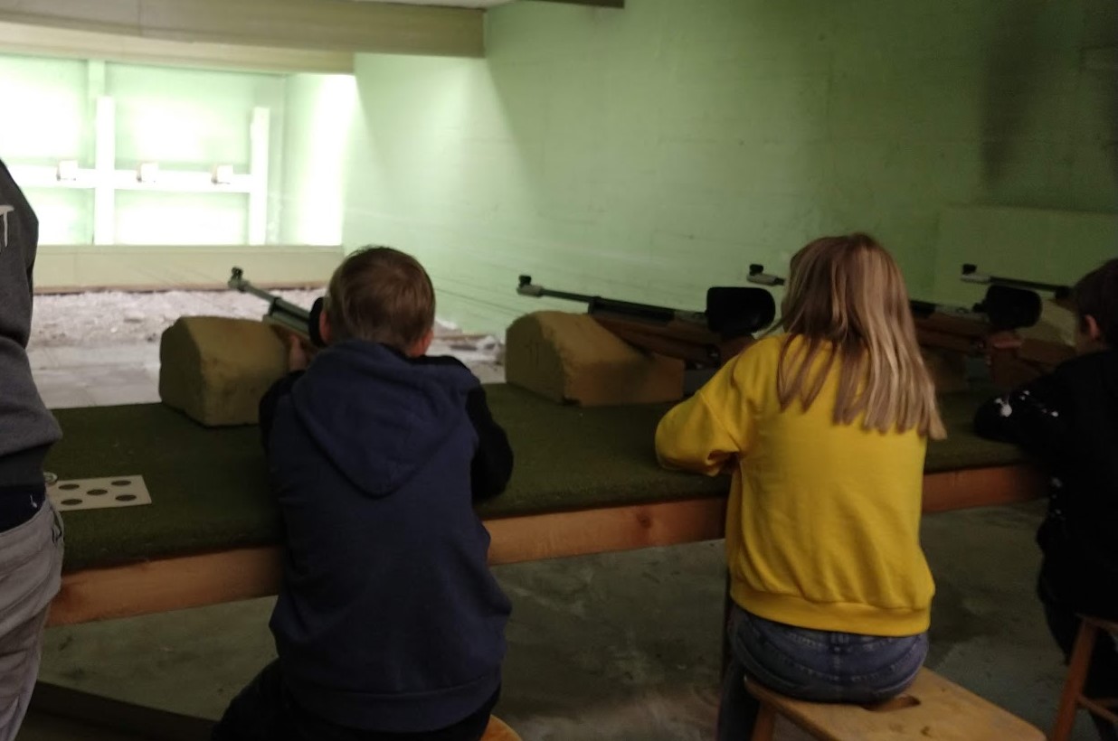 två barn skjuter luftgevär i en skyttehall