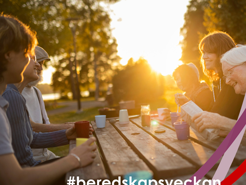 människor sitter vid ett bord utomhus i motljus, gröna träd och solen i bakgrunden