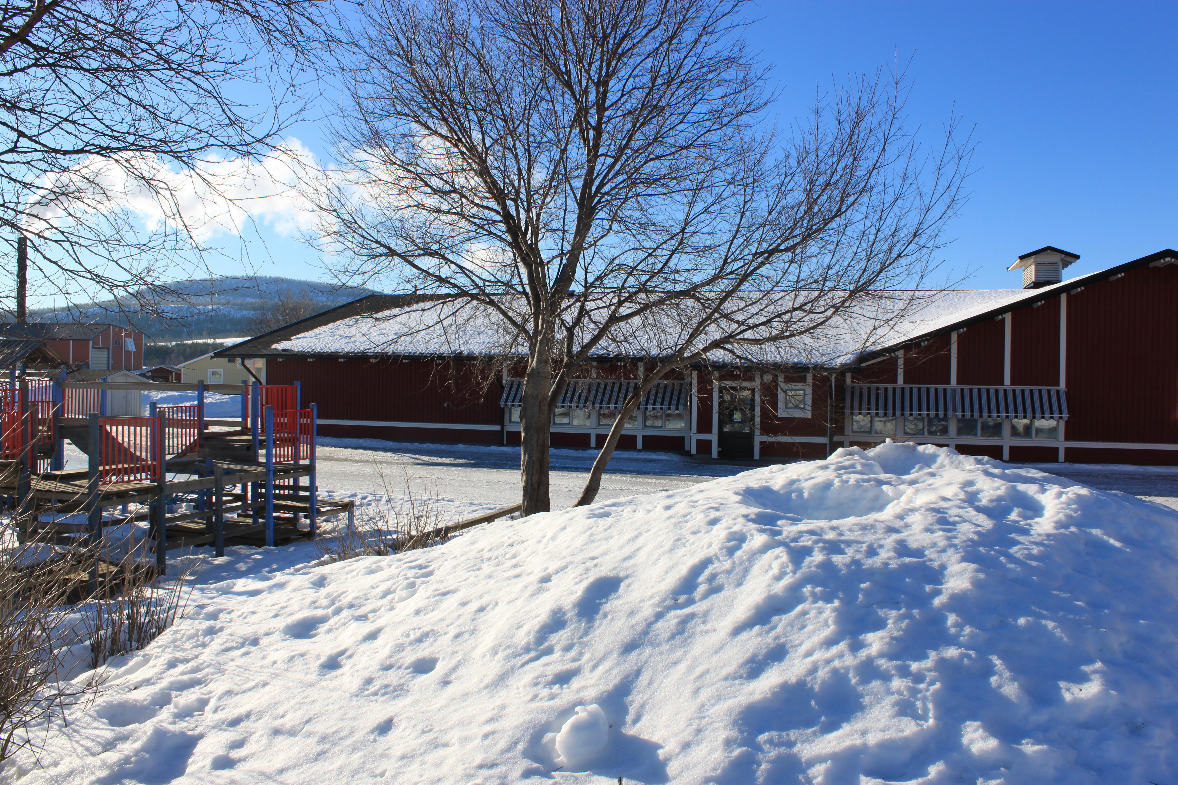 röd skolbyggnad omgiven av snöhögar och kala träd