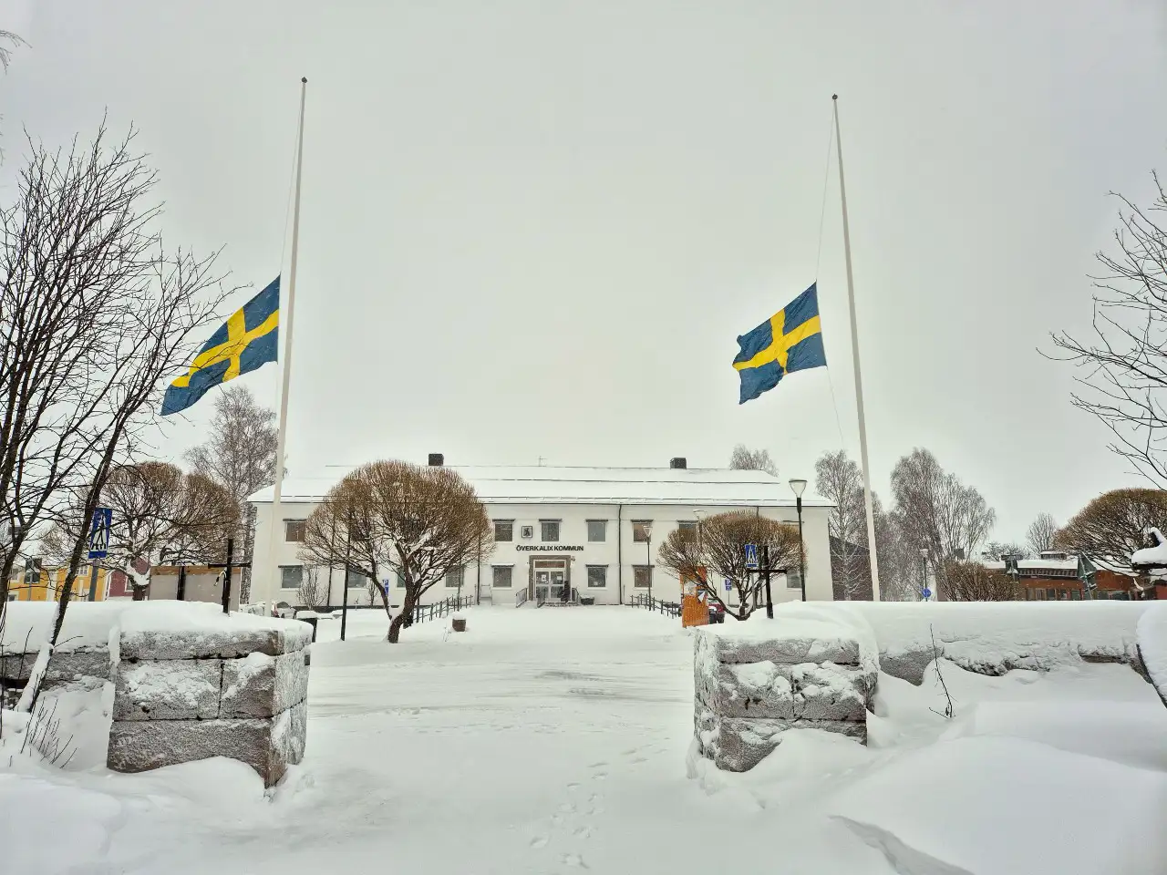 ett vitt hus i bakgrund med två flaggstänger framför där flaggorna hänger på halv stång