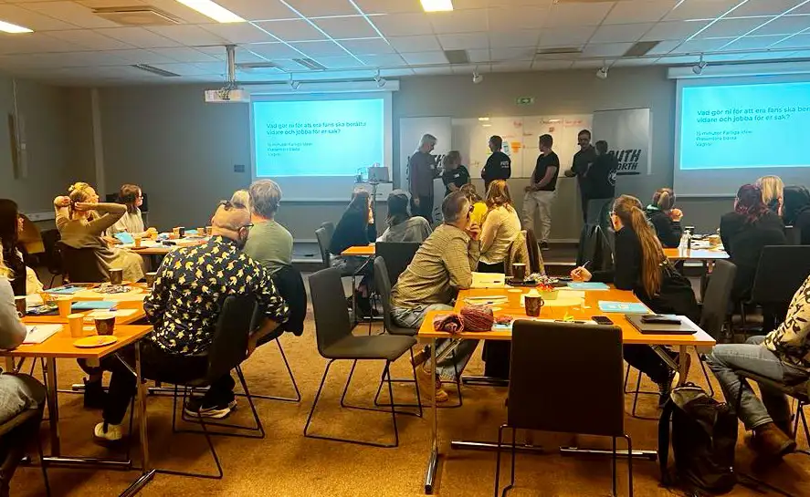 ett konferensrum med deltagare sittande vid olika bord