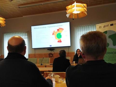 Ett antal personer sitter i ett konferensrum och ser på en presentation på en skärm på väggen