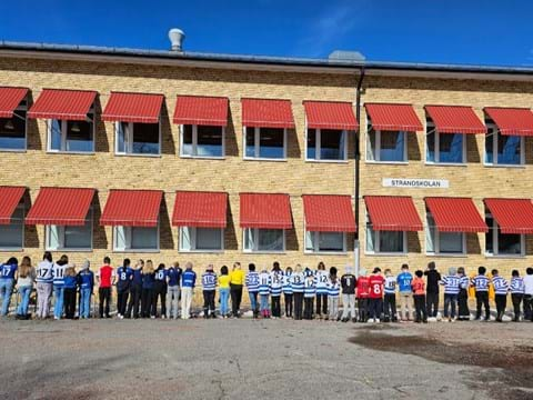 elever i fotbollströjor står med ryggarna mot kameran framfrö en gul tegelskola med röda markiser