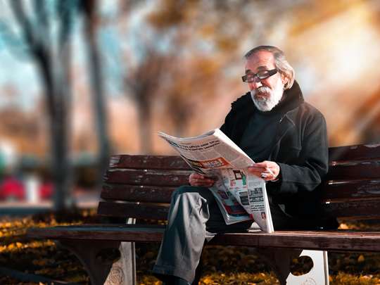 Äldre man som sitter och läser på en bänk utomhus