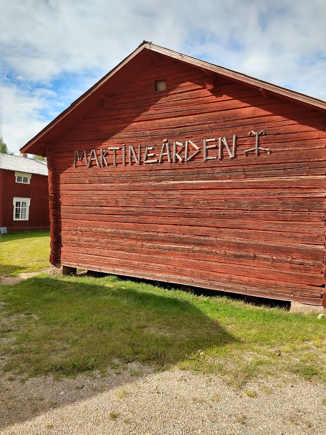 bilden visar gaveln på ett av Martingårdens uthus, ett rött timmrat enplanshus