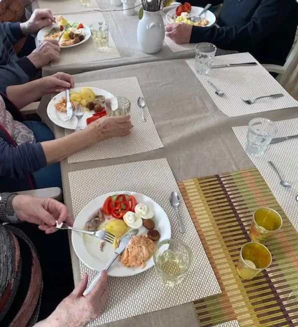 bild på dukat bord med påskbuffé, vita tallrikar med mat och händer på personerna som sitter till bords