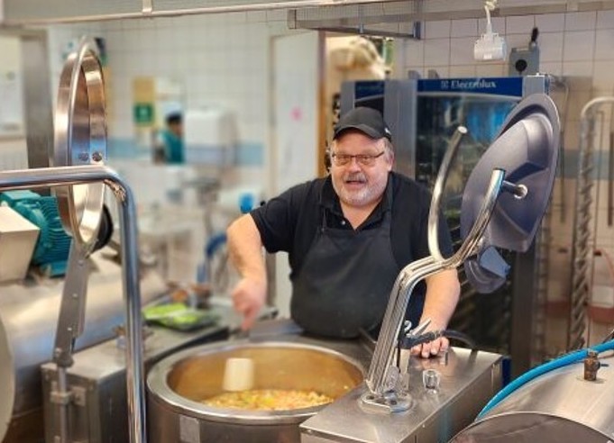 en man i kockkläder rör i en stor gryta i ett storkök