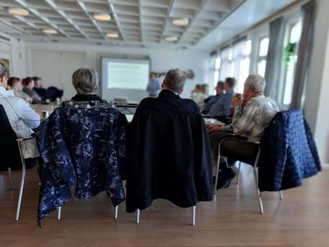 bilden visar ett antal personer som sitter runt ett bord och lyssnar på en föreläsare
