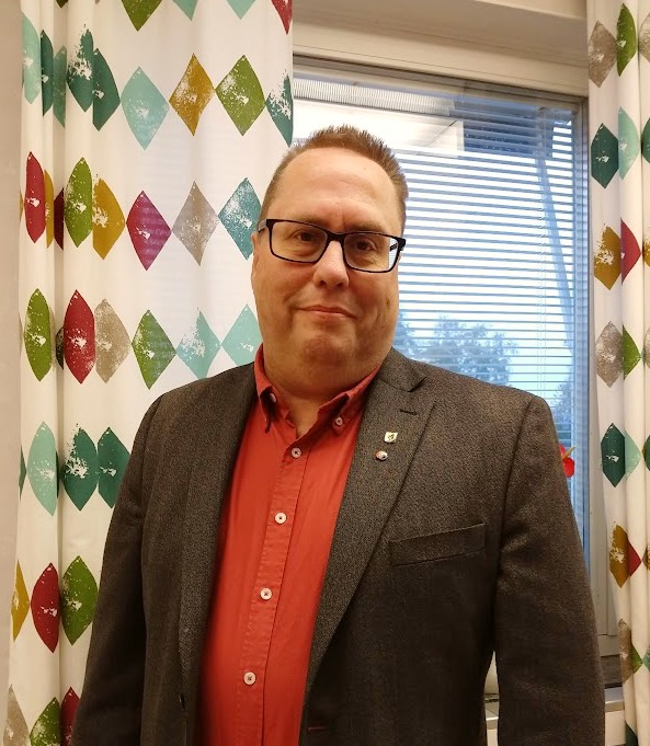 man i röd skjorta och grå kavaj framför ett fönster