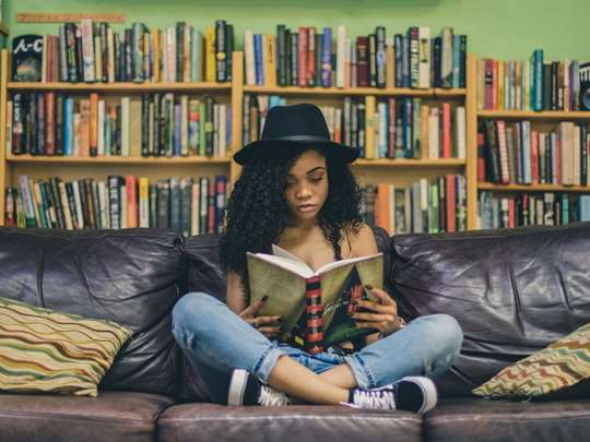 bilden visar en flicka med korslagda ben i en soffa med en bok i handen och bokhyllor i bakgrunden