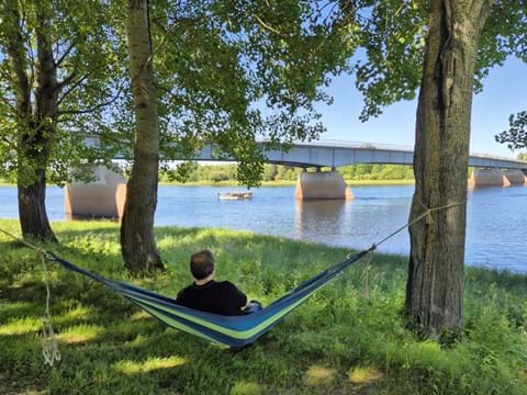 man sitter i en hängmatta mellan två grönskande träd och Kalix älv framför sig