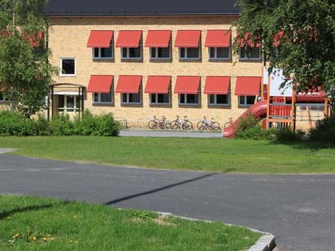 Sommarbild skolgård och tegelbyggnad med röda markiser i bakgrunden. 