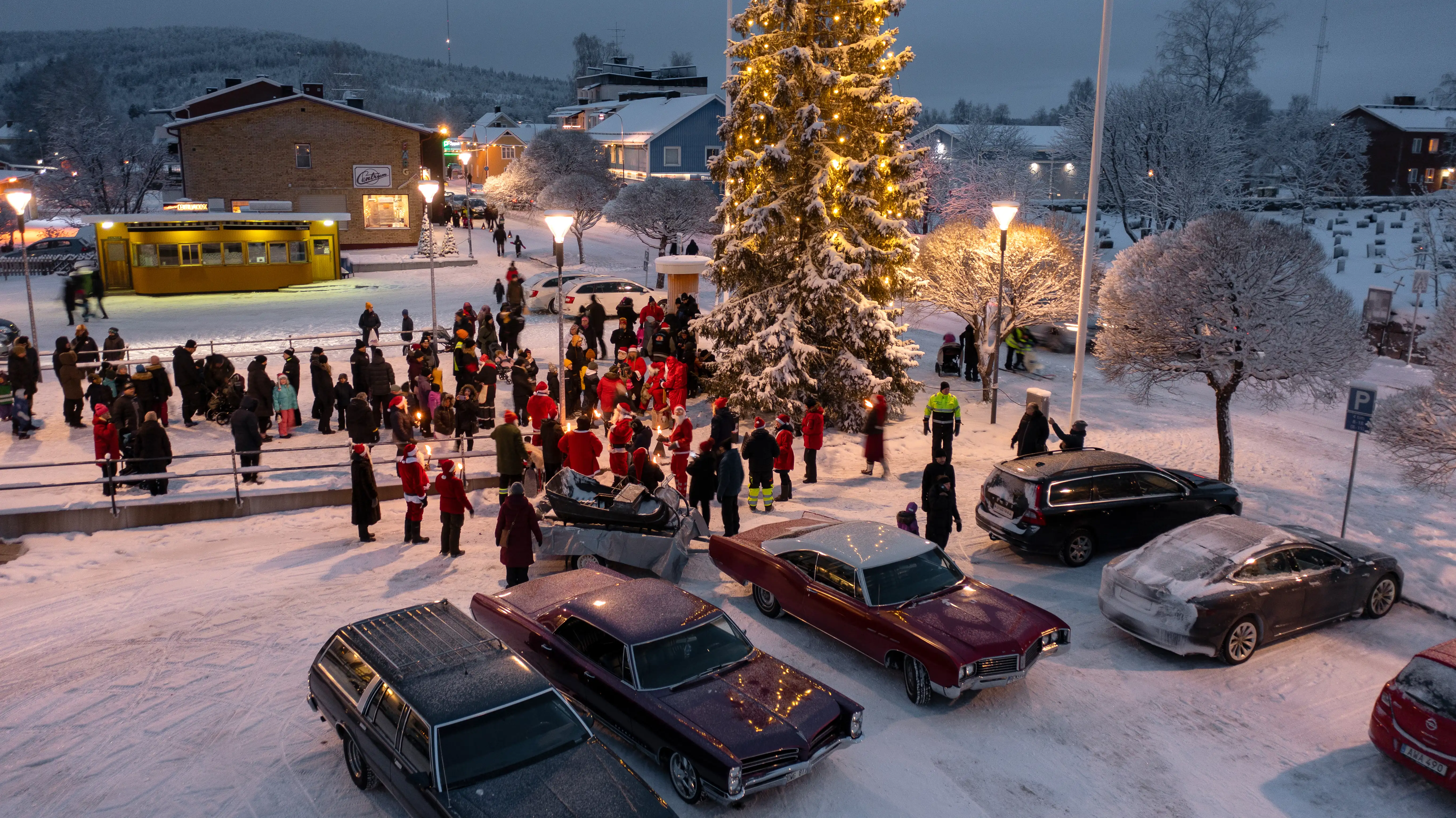 bilden visar människor och bilar på ett snöigt torg med en julgran