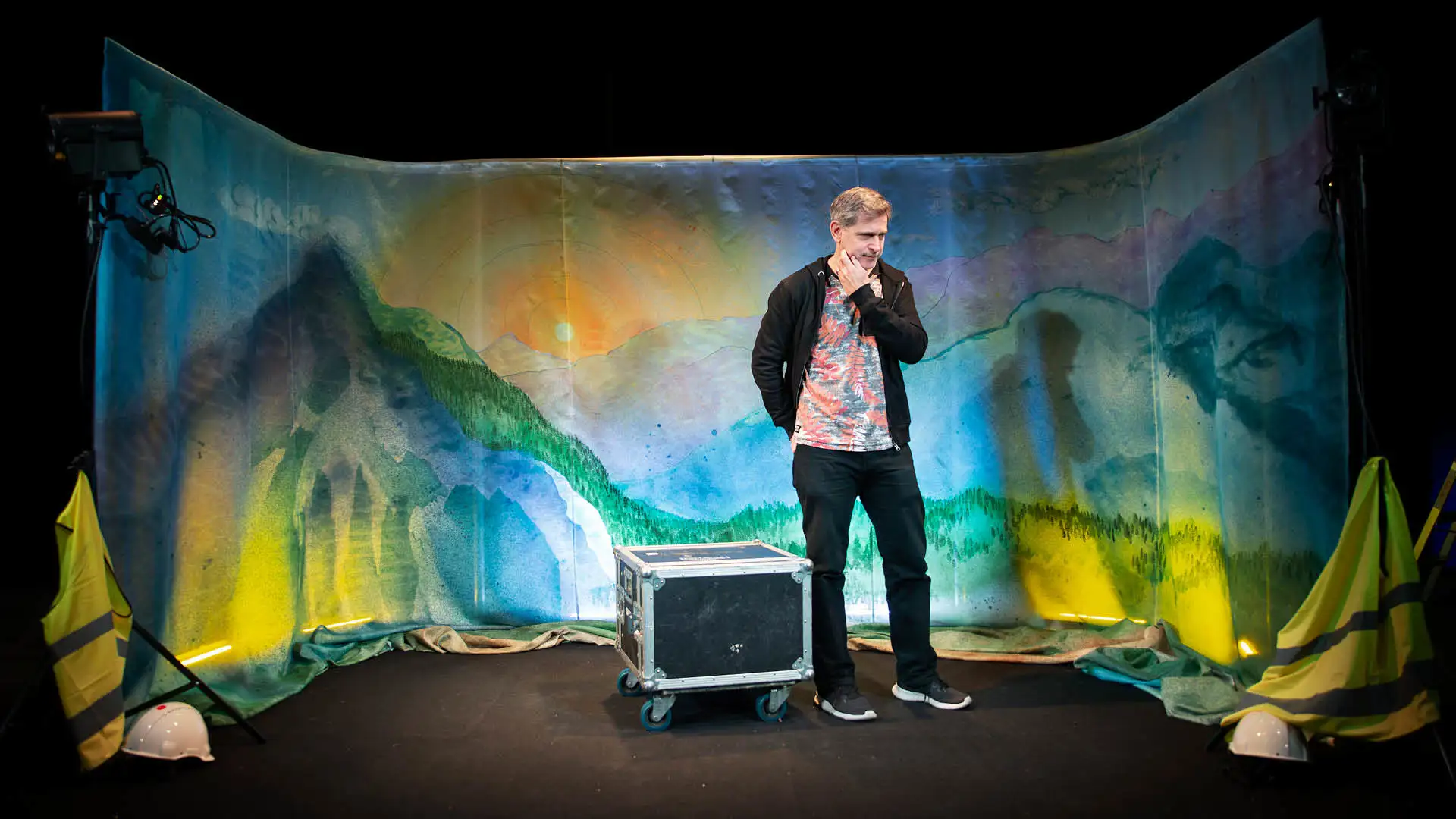 bilden visar en manlig skådespelare på en scen med ett målat landskap i bakgrunden